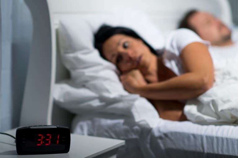 A woman awake looking at a clock reading 3:31
