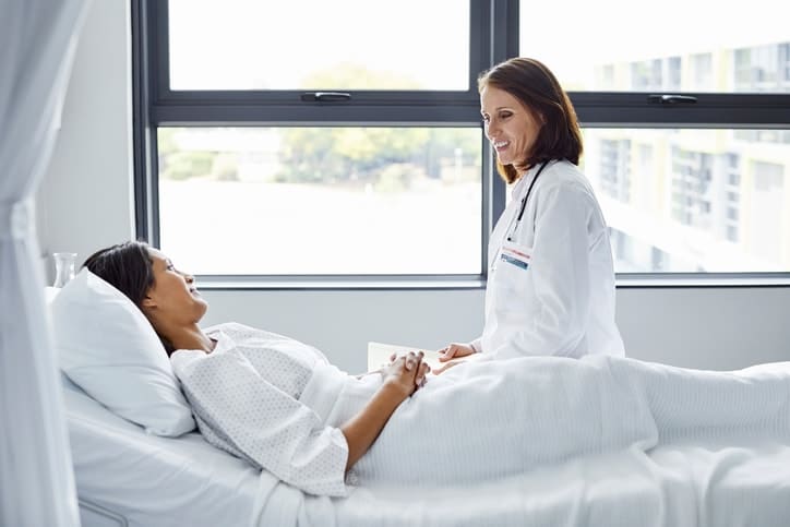 Smiling doctor looking at patient lying in bed