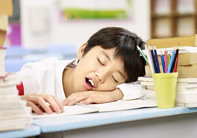 student tired falling asleep on desk in school