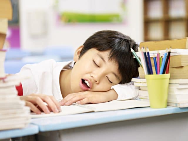 student tired falling asleep on desk in school