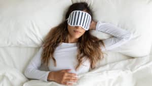 Calm peaceful young lady wearing sleeping mask, dreaming.