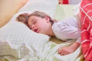 face of blonde caucasian five years old girl, with open mouth and funny expression sleeping on king bed