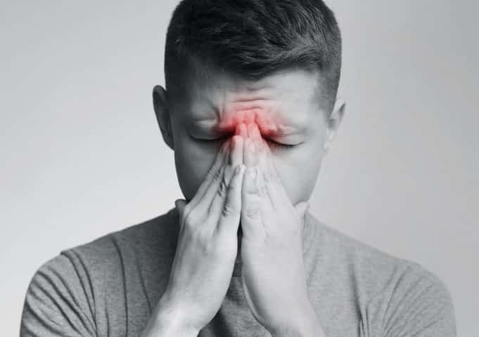 Sinus pain, sinusitis. Sad man holding his nose, black and white photo with red sore zone