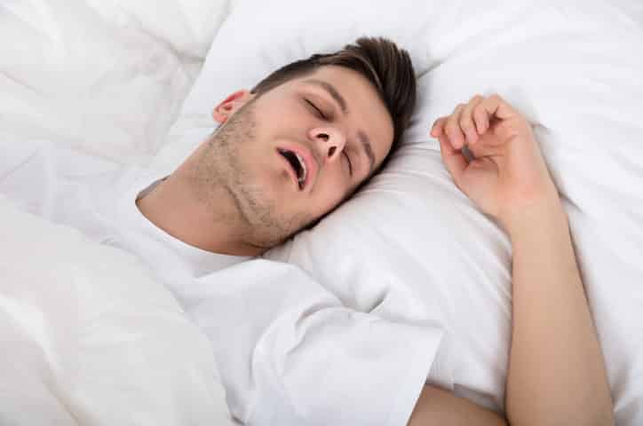 View Of Tired Young Man Snoring While Deep Sleeping In Bed